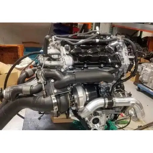 A performance turbo kit installed on an engine, featuring metallic and black components including downpipes and turbocharger.